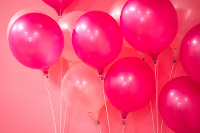 a large number of hot pink and light pink balloons with white strings hanging down.